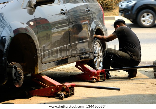Chiang rai, Thailand - March 18,2019:The\
mechanic wears a black short-sleeved shirt, a left arm with a\
tattoo, removing the tire from the\
car.