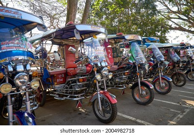 Chiang Saen, Chiang Rai Province, Thailand - February 19, 2019: Traditional Thai auto rickshaws (tuk-tuk) of different colors stand in a row waiting for passengers. Thai northeast style tuk-tuk