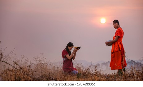 CHIANGMAI, THAILAND – FEBRUARY 26: A young woman wearing a red hill tribe wearing dress and food in the alms bowl for the monks on the morning of the day on February 26, 2020 in Chiangmai, Thailand.