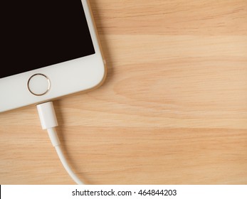 CHIANGRAI, THAILAND -JULY 28, 2016: Top view image of the Apple iPhone 6 charging with Lightning USB Cable on the wooden table on July 28, 2016 in Chiangrai Thailand.