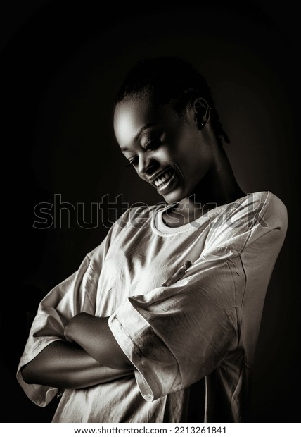 A chiaroscuro image with a\
young black lady smiling, there is a contrast of light and\
darkness