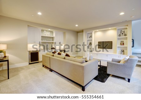Chic basement features a gray sectional facing a white built-in tv cabinet and wet bar mounted to a wall. Northwest, USA
