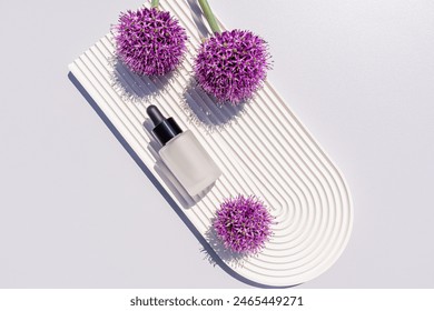 A chic bottle with a cosmetic serum for face skin care on a white tray in the form of arch among purple alliums. top view. Beauty and care concept. - Powered by Shutterstock