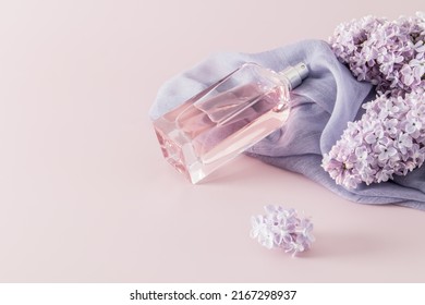 a chic bottle of women's perfume or eau de parfum lies on a woman's accessory - a scarf and lilac flowers. space for text. pink background