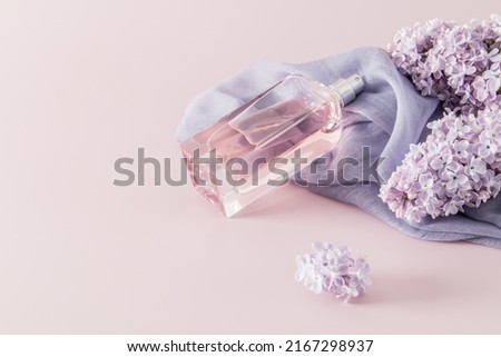 a chic bottle of women's perfume or eau de parfum lies on a woman's accessory - a scarf and lilac flowers. space for text. pink background
