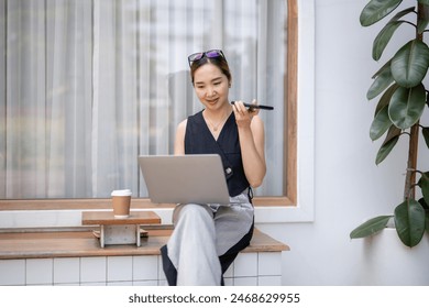 Chic businesswoman with sunglasses using voice assistant on her phone while working on a laptop in a modern office setting.

 - Powered by Shutterstock