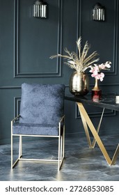 Chic dark interior showcases a plush navy chair with gold legs next to a modern table with decorative vases and elegant floral arrangements enhancing the atmosphere