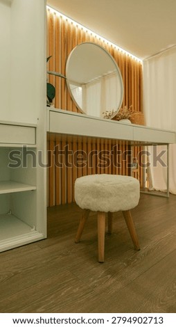 A chic dressing area featuring a sleek white vanity, a plush circular stool, and a decorative mirror against a slatted wood wall