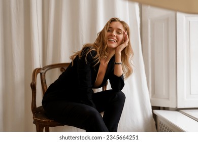 Chic and Elegant: Gorgeous Woman with Wavy Hair posing in stylish light appartments. Wearing  casual  black outfit. 