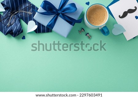 Chic Father's Day arrangement. Overhead shot of postcard, ribbon-tied giftbox, necktie, cufflinks, spectacles, paper hearts, coffee mug on teal backdrop with space for text