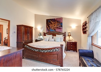 Chic Master Bedroom Features Vaulted Ceiling Over Gorgeous Wood Carved Bed, Cabinet, Two Nightstands And Black Leather Tufted Bench By The Window. Northwest, USA