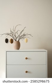 Chic minimalist easter decor features dry branches with craft eggs elegantly arranged in a simple vase, easter rabbit set a top a modern dresser. High quality photo