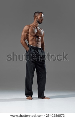 Chic and powerful. Image of young athletic man in loose, dark trousers, showing perfect blend of athleticism and casual style. Concept of beauty and fashion, style and youth, male health.