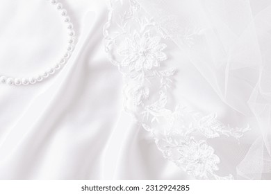Chic wedding background for design. white satin fabric with soft waves, lace embroidered bridal veil and pearl necklace