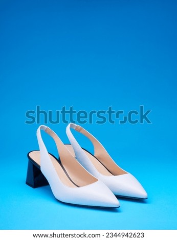 Chic white pointed-toe female shoes with an open back and black flare heels on a gradient blue background with copy space. Creative minimalistic layout with footwear.