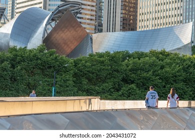 Chicago, IL - September 16, 2021: A young couple walks along the BP Bridge that connects Millennium Park and Maggie Daley Park, downtown in the Loop, with a view of Pritzker Pavilion beyond.