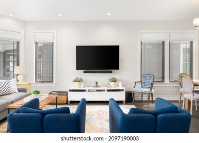 CHICAGO, IL, USA - APRIL 7, 2021: A Cozy Living Room With Blue Chairs Sitting In Front Of A Mounted Television, An Area Rug On Hardwood Floors, And Windows.