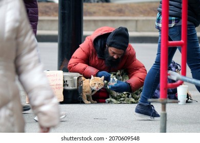 Chicago, IL, USA - december 24th 2020: Homeless man with his ginger cat looking in the camera viewed on State street in Chicago on Christmas eve