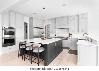 CHICAGO, IL, USA - FEBRUARY 28, 2021: A Luxurious Kitchen With A Large Island, Gold Faucet And Sputnik Chandelier, Stainless Steel Appliances, And White Marble Countertops.