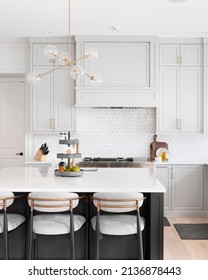 CHICAGO, IL, USA - FEBRUARY 28, 2021: A Luxurious Kitchen With A Large Island, Gold Faucet And Sputnik Chandelier, Stainless Steel Appliances, And White Marble Countertops.