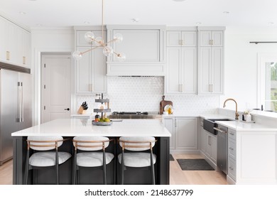 CHICAGO, IL, USA - FEBRUARY 28, 2021: A Luxurious Kitchen With A Large Island, Gold Faucet And Sputnik Chandelier, Stainless Steel Appliances, And White Marble Countertops.