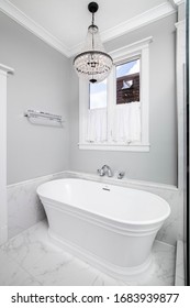 CHICAGO, IL, USA - FEBRUARY 6, 2020: A Luxurious, White Stand Alone Tub With A Chandelier Hanging From The Ceiling A Blue Sky Through The Window.