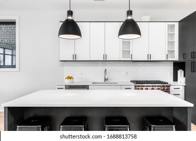 CHICAGO, IL, USA - FEBRUARY 8, 2020: A Modern Kitchen With Black And White Cabinets, Stainless Steel Wolf And Sub-Zero Appliances, And Bar Stools Sitting At The White Granite Counter Top.