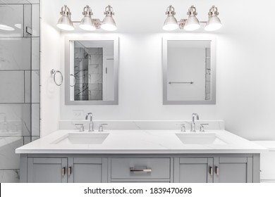 CHICAGO, IL, USA - JANUARY 2, 2020:  An elegant, remodeled bathroom with a grey vanity and bronze hardware. The shower has a large shower head and marble tiles and glass wall line the sides.