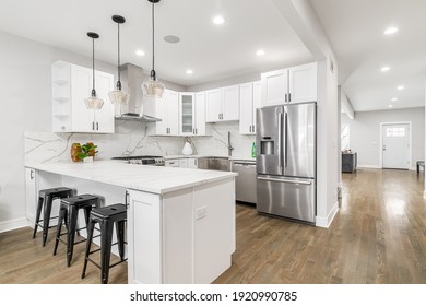 CHICAGO, IL, USA - JANUARY 22, 2020: A new, modern all white kitchen with black lights hanging from the ceiling and black bar stools sitting at the counter top for an eating area. Lights on.