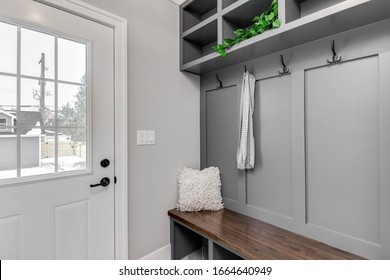 CHICAGO, IL, USA - JANUARY 27, 2020: A staged detail shot of a gray mudroom / entryway with bench seating, coat hooks, and storage above. A scarf hangs from a hook and a plant sitting on a shelf.
