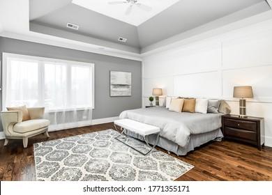 CHICAGO, IL, USA - JANUARY 27, 2020: A neutral colored, large master bedroom with high ceilings and molding squares on the wall. The room features a king bed, decorated nightstands, and a bench seat.