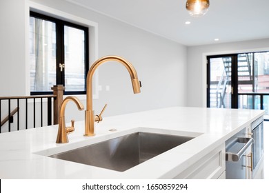 CHICAGO, IL, USA - JANUARY 4, 2020: A Gold Kitchen Faucet Detail Shot With An All White Kitchen, A Gold Light Hanging From The Ceiling With A Living Room In The Background.