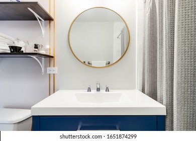 CHICAGO, IL, USA - JANUARY 4, 2020: A Simple Bathroom With A Blue Vanity And White Marble Counter Top. Shelving Is Mounted Aside A Gold, Round Mirror.