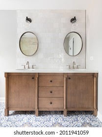 CHICAGO, IL, USA - JULY 3, 2021: A cozy bathroom with a patterned tile floor, natural wood vanity, tiled backsplash, and lights mounted above circular mirrors.