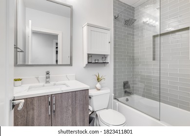 CHICAGO, IL, USA - JUNE 16, 2020: A small bathroom with a white marble counter top, wood cabinet, and a custom tiled shower with a shelf.