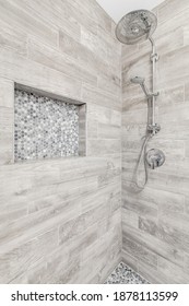 CHICAGO, IL, USA - JUNE 16, 2020: A Renovated Shower With Brown Marble Tiles Lining The Walls, A Shelf With Small Mosaic Tiles, And A Chrome Shower Head.