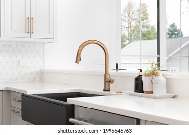 CHICAGO, IL, USA - JUNE 2, 2021: A beautiful sink in a remodeled modern farmhouse kitchen with a gold faucet, black apron or farmhouse sink, white granite, and a tiled backsplash.