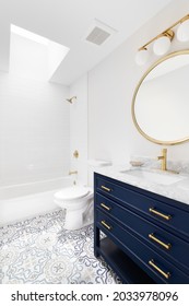 CHICAGO, IL, USA - JUNE 27, 2021: A White Bathroom With A Blue Vanity Cabinet, Granite Countertop, Pattern Tile Flooring, And Gold Fixtures And Mirror.