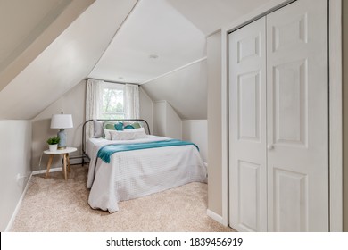 CHICAGO, IL, USA - JUNE 28, 2020: A Cozy, Slanted Ceiling Bedroom, A Lamp On The Nightstand Beside The Bed, And A Large Closet Door.