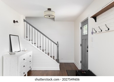 CHICAGO, IL, USA - JUNE 28, 2021: An Foyer In A Farmhouse Style Home With Shiplap On The Wall, A Staircase With A Grey Banister And White Spindles, And A Grey Door.