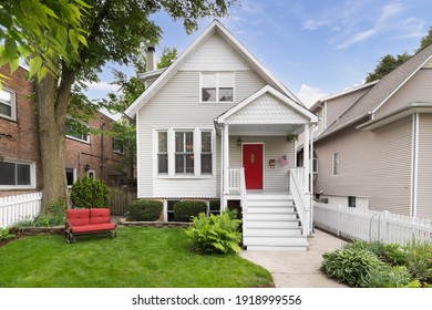 CHICAGO, IL, USA - JUNE 3, 2019: A Beautiful White House With A Small Front Porch And Red Front Door Surrounded Be A Nicely Landscaped Yard And White Picket Fence.