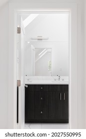 CHICAGO, IL, USA - JUNE 3, 2021: Looking Towards A Bathroom Through The Door Way With A Dark Wood Vanity Cabinet, White Granite Countertop, And Light Above The Mirror.