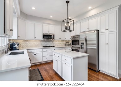 CHICAGO, IL, USA - JUNE 30, 2019: A Bright Kitchen With White Cabinets, White Granite Counter Tops, Stainless Steel Appliances And Light Fixture Hanging Over The Island.