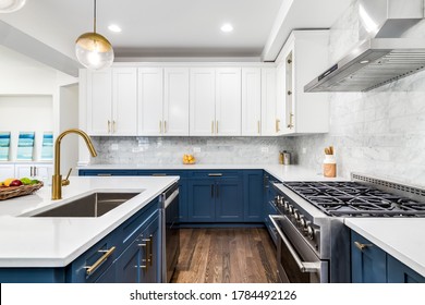 CHICAGO, IL, USA - JUNE 7, 2020: A luxurious white and blue kitchen with gold hardware, Bosch and Samsung stainless steel appliances, and white marbled granite counter tops.