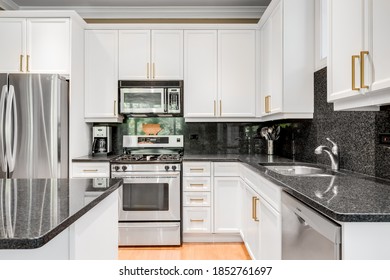 CHICAGO, IL, USA - JUNE 7, 2020: A White Kitchen With A Black Granite Counter Top And Back Splash, Stainless Steel Appliances, And Hardwood Floors.