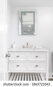 CHICAGO, IL, USA - JUNE 7, 2020: A New Bathroom With Chrome Hardware And Faucet, A Lit Mirror, White Cabinet, And White Marble Counter Top.