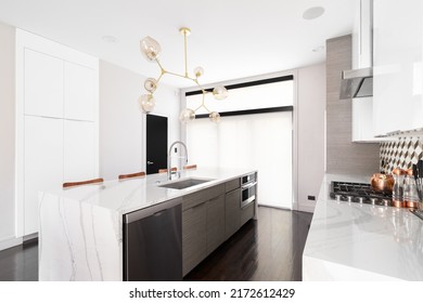 CHICAGO, IL, USA - MARCH 4, 2022: A Beautiful, Modern Kitchen With A Gold Light Fixture Above A Waterfall Granite Island, Stainless Steel Appliances, And A Tiled Backsplash.