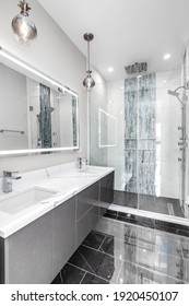 CHICAGO, IL, USA - NOVEMBER 1, 2020: A Modern, Luxury Bathroom With A White Granite Countertop, Grey Vanity Cabinet, Hinckley Pineapple Light Fixtures Hanging Above, And A Marble And Glass Shower.