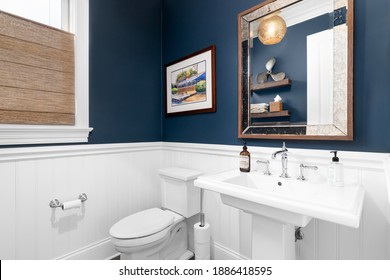 CHICAGO, IL, USA - OCTOBER 12, 2020: A Small, Classic Blue And White Paneled Bathroom With A White Pedestal Sink, Gold Light Fixture Hanging From The Ceiling, And Chrome Faucet.