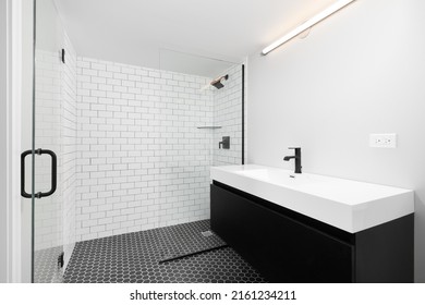 CHICAGO, IL, USA - OCTOBER 4, 2021: A Renovated Bathroom With A Black Vanity Cabinet, White Vessel Sink And Black Faucet, Black Hexagon Tile Flooring, And A White Subway Tile Shower.